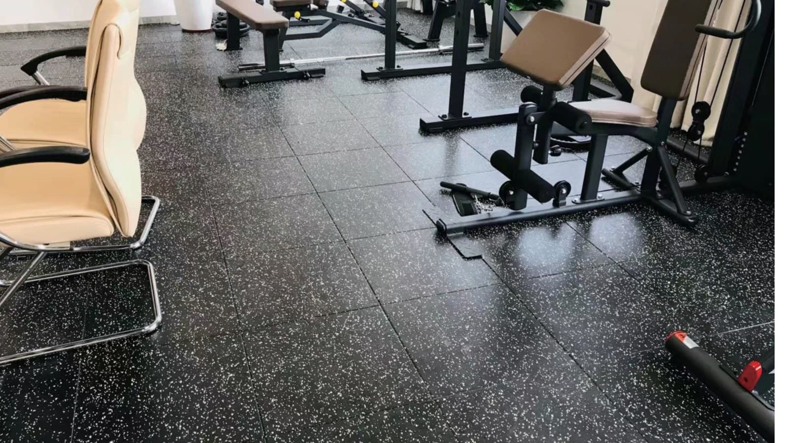 Gym rubber flooring with black speckled rubber floor tiles in a fitness area.