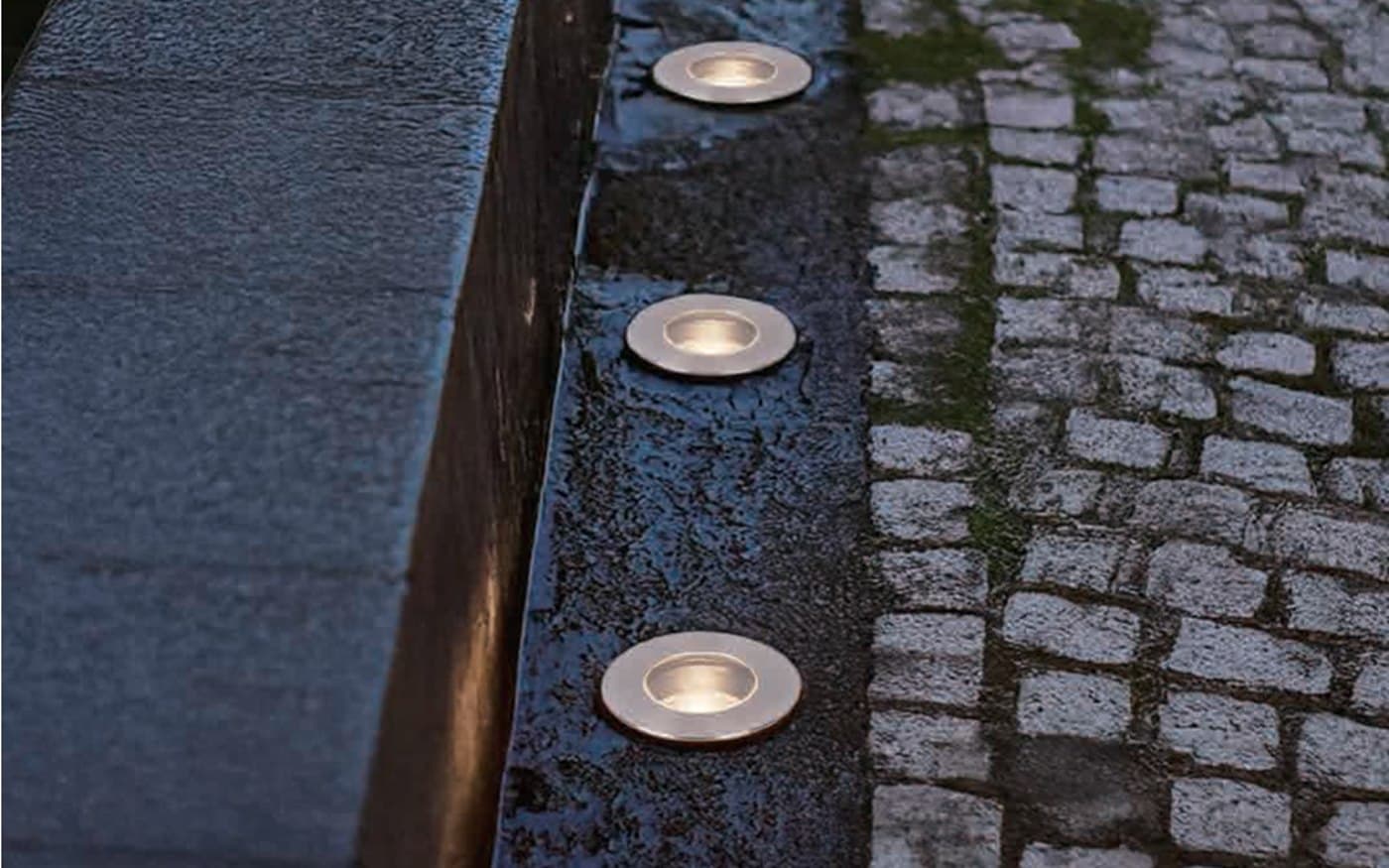 In-ground exterior lights placed along a paved pathway edge.